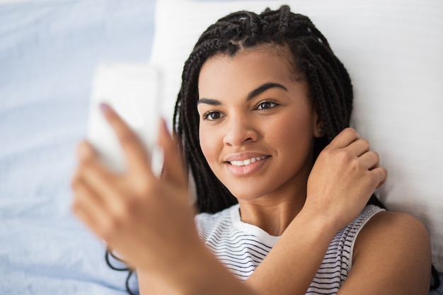 Mujer bastante africana haciendo selfie en la cama