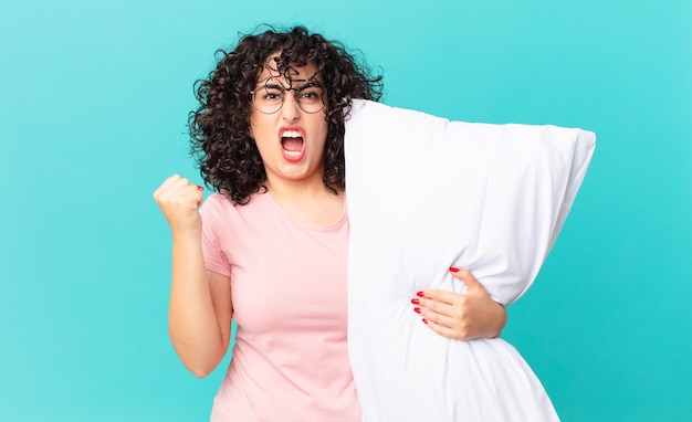 Foto mujer bastante árabe gritando agresivamente con una expresión enojada. en pijama y sosteniendo una almohada