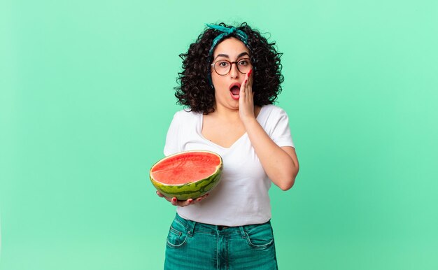 Mujer bastante árabe sintiéndose conmocionada y asustada y sosteniendo una sandía. concepto de verano