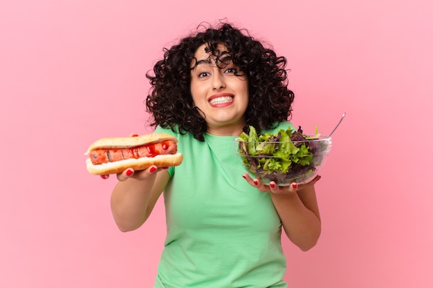 Mujer bastante árabe sosteniendo una ensalada y un perrito caliente. concepto de dieta