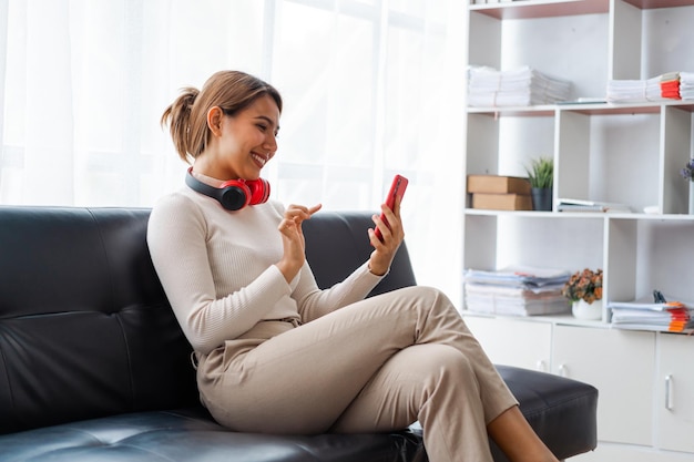 Mujer bastante asiática que usa teléfono móvil cuando se sienta en el sofá en casa