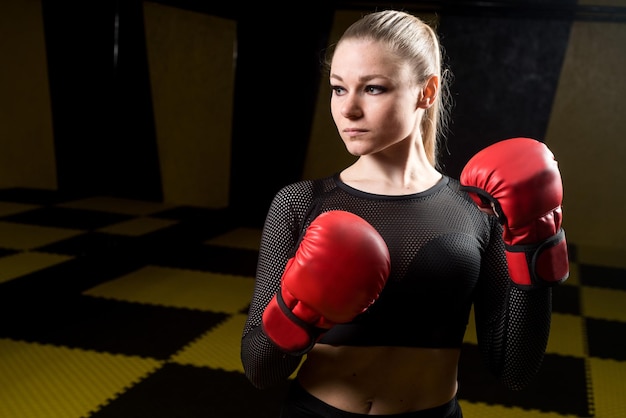 Mujer bastante atlética en guantes de boxeo rojos posando en el gimnasio