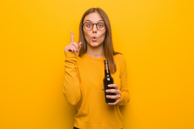 Mujer bastante caucásica joven que tiene una gran idea, concepto de creatividad. Ella está sosteniendo una cerveza.