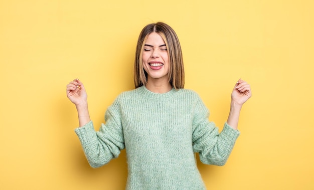 Mujer bastante caucásica que parece extremadamente feliz y sorprendida celebrando el éxito gritando y saltando