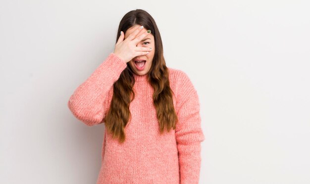 Mujer bastante caucásica que parece sorprendida asustada o aterrorizada cubriendo la cara con la mano y mirando entre los dedos