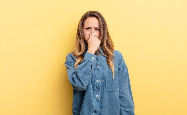 Mujer bastante caucásica que se siente disgustada tapándose la nariz para evitar oler un hedor desagradable y desagradable