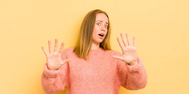 Mujer bastante caucásica que se siente estupefacta y asustada temiendo algo aterrador con las manos abiertas al frente diciendo que se mantenga alejado