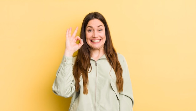 Mujer bastante caucásica que se siente exitosa y satisfecha sonriendo con la boca abierta haciendo un buen signo con la mano