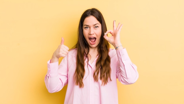 Mujer bastante caucásica sintiéndose feliz asombrada satisfecha y sorprendida mostrando gestos de aprobación y pulgares arriba sonriendo