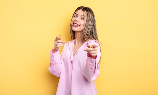 Mujer bastante caucásica sonriendo con una actitud positiva, exitosa y feliz apuntando a la cámara, haciendo señales de armas con las manos