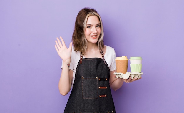 Mujer bastante caucásica sonriendo alegremente agitando la mano dándole la bienvenida y saludando el concepto de café para llevar