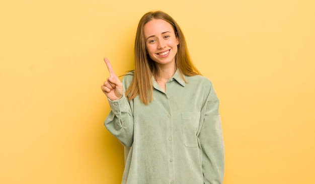 Mujer bastante caucásica sonriendo y luciendo amigable mostrando el número uno o primero con la mano hacia adelante contando hacia atrás