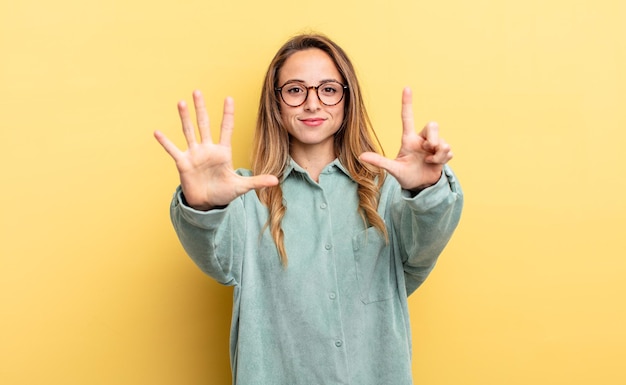 Foto mujer bastante caucásica sonriendo y luciendo amigable, mostrando el número siete o séptimo con la mano hacia adelante, contando hacia atrás