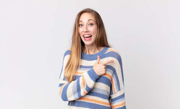 Mujer bastante delgada que parece emocionada y sorprendida apuntando hacia un lado y hacia arriba para copiar espacio