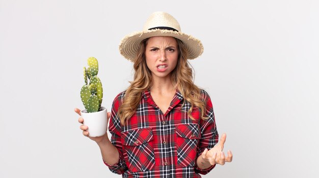Mujer bastante delgada que parece enojada, molesta y frustrada sosteniendo un cactus. concepto de granjero
