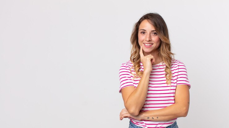 Foto mujer bastante delgada que parece feliz y sonriente con la mano en la barbilla, preguntándose o haciendo una pregunta, comparando opciones