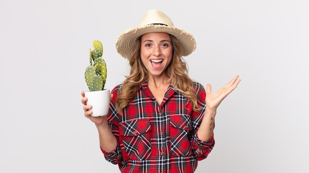 Mujer bastante delgada que se siente feliz y asombrada por algo increíble sosteniendo un cactus. concepto de granjero