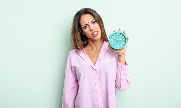 Foto mujer bastante hispana que se siente perpleja y confundida. concepto de reloj despertador