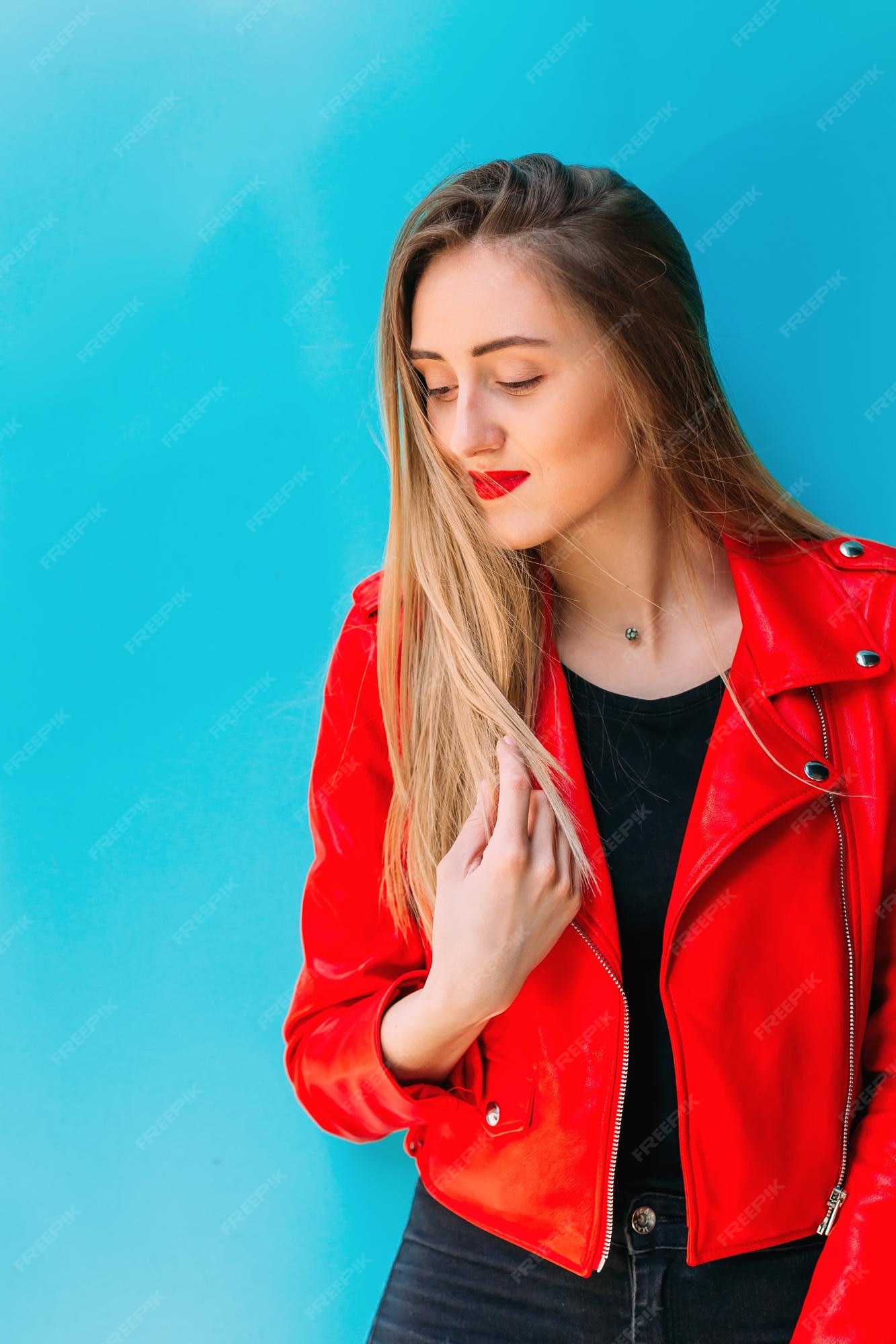 Mujer bastante joven chaqueta de cuero roja junto a una pared azul | Foto Premium