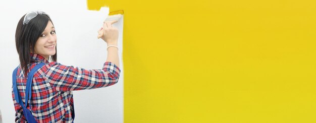 La mujer bastante joven pinta el color amarillo de la pared, bandera horizontal de la foto