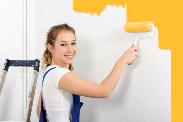 La mujer bastante joven pinta la pared en naranja