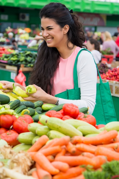 Mujer bastante joven que compra verduras en el mercado