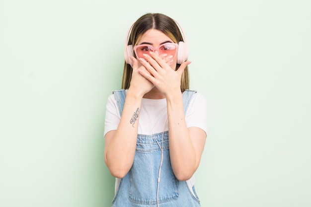 Mujer bastante joven que cubre la boca con las manos con una sorpresa. escuchar música concepto