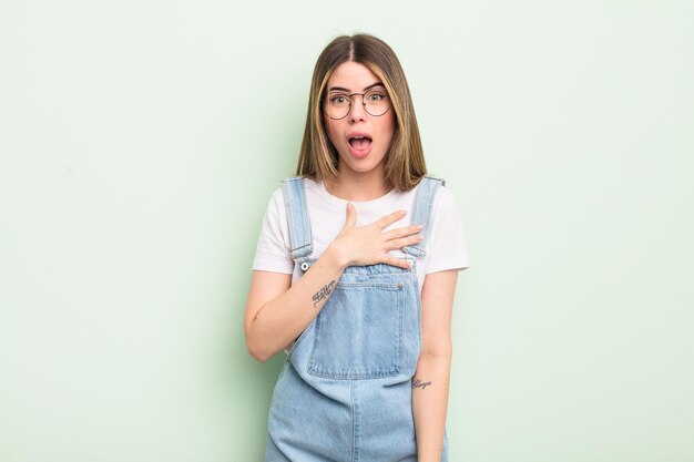 Mujer bastante joven que se siente conmocionada y sorprendida, sonriendo, tomándose las manos en serio, feliz de ser la indicada o mostrando gratitud