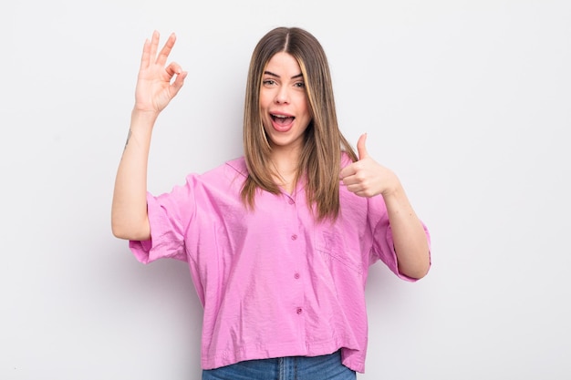 Mujer bastante joven que se siente feliz, asombrada, satisfecha y sorprendida, mostrando gestos de aprobación y aprobación, sonriendo