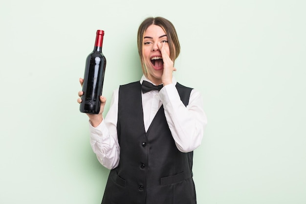 Mujer bastante joven que se siente feliz, dando un gran grito con las manos junto a la boca. concepto de camarero y botella de vino