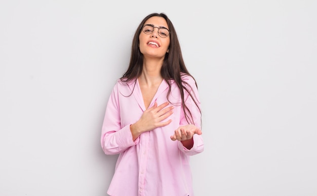 Mujer bastante joven que se siente feliz y enamorada sonriendo con una mano al lado del corazón y la otra estirada al frente