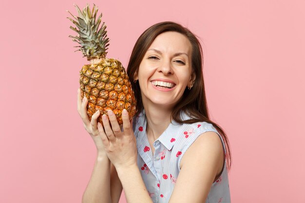 Mujer bastante joven con ropa de verano sosteniendo en las manos fruta fresca de piña madura aislada en un fondo de pared rosa pastel en el estudio. Estilo de vida vivo de la gente, concepto de vacaciones relajantes. Simulacros de espacio de copia.