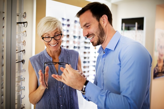 Mujer bastante madura está eligiendo gafas nuevas en la tienda de óptica