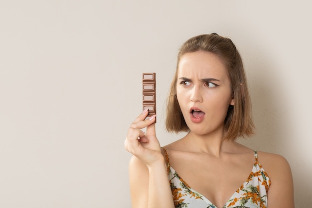 Mujer bastante morena agitada sosteniendo una pequeña barra de chocolate. Espacio vacio