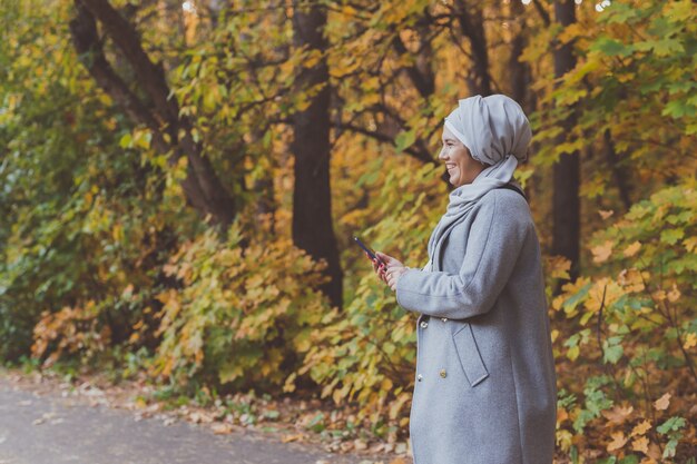 Mujer bastante musulmana con teléfono móvil al aire libre. Mujer árabe con hijab con smartphone. Chica islámica enviando un mensaje de texto a un teléfono en el parque de la ciudad. Copia espacio