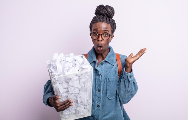 Mujer bastante negra que parece sorprendida y conmocionada con la mandíbula caída sosteniendo un concepto de falla de bolas de papel de objeto