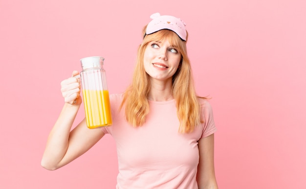 Mujer bastante pelirroja en pijama y sosteniendo un jugo de naranja. concepto de desayuno saludable