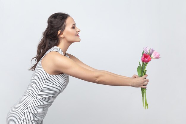 Mujer bastante positiva sosteniendo un ramo de tulipanes entregándoselo a su madre felicitándola por el mes de marzo.