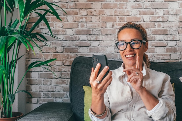 Mujer bastante rizada feliz tomando una foto selfie en el teléfono móvil en casa usando el servicio virtual de la aplicación en línea para hacer llamadas de pago Usuario de teléfono celular satisfecho chateando navegando en internetxA