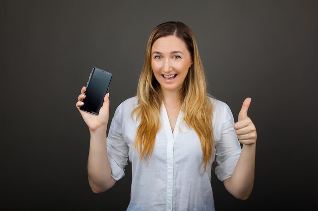 Mujer bastante sonriente que muestra una pantalla vertical en blanco del teléfono inteligente