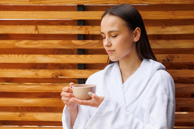 Mujer en bata de baño bebiendo té matutino en la terraza