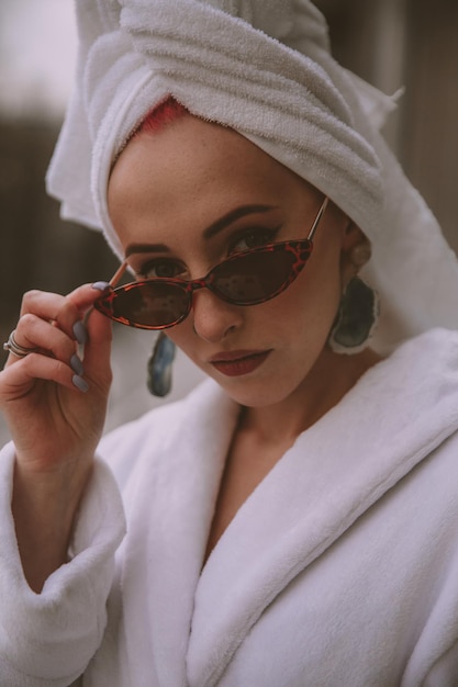 Foto mujer en bata de baño blanca y gafas de sol mira a los ojos