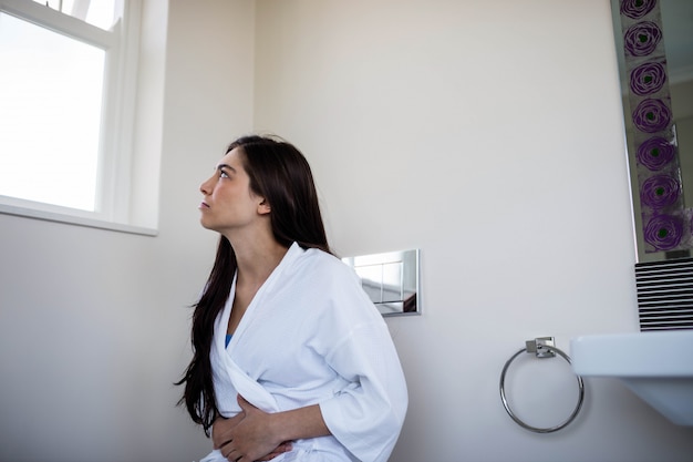 Mujer en bata de baño con dolor de barriga en el baño