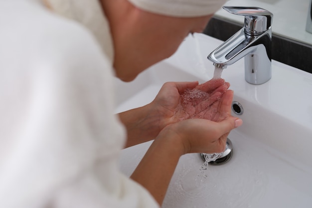 Mujer en bata de baño se lava la cara con agua limpia