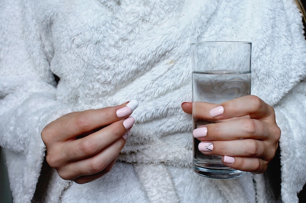 Mujer en una bata de baño con una pastilla y un vaso de agua