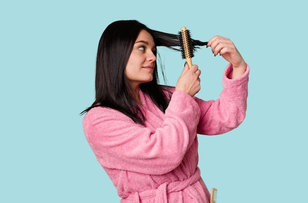 Mujer en bata de baño rosa preparándose para arreglarse el cabello con un peine luciendo bonita y preparada