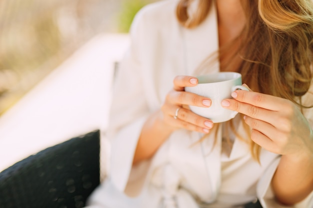 Una mujer en una bata por la mañana se sienta en una silla y sostiene una taza en sus manos