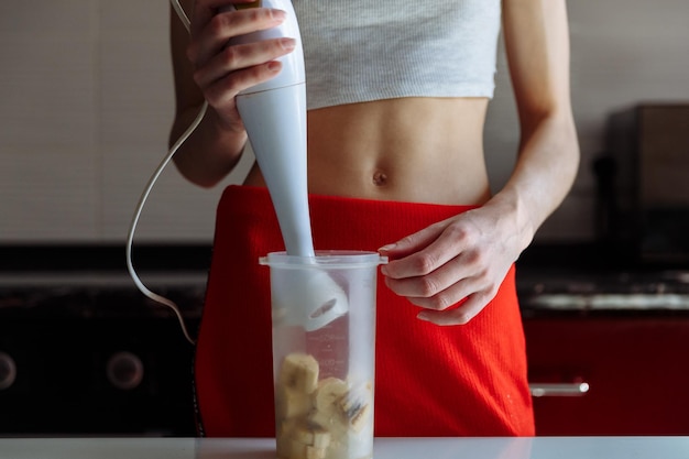 Mujer con batidora de mano haciendo polvo de proteína de plátano dulce batido batido de proteína después del entrenamiento dieta de nutrición deportiva después del gimnasio Estilo de vida saludable