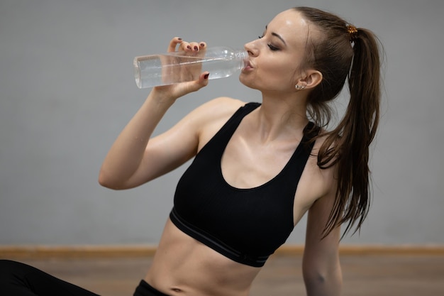 Mujer bebe agua después de hacer ejercicio en el gimnasio
