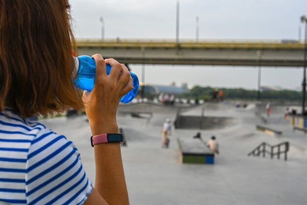 Una mujer bebe agua después de montar en un parque extremo. De cerca. El parque de patinaje, rollerdrome, rampas de cuarto y medio tubo. Deporte extremo, cultura urbana juvenil para la actividad callejera de los adolescentes.